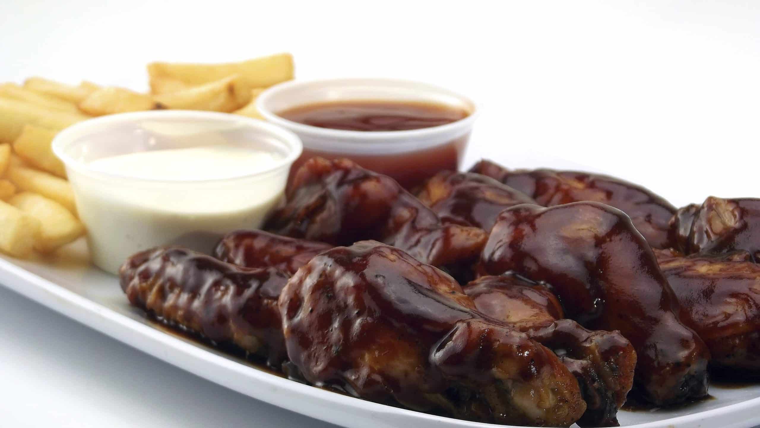 Plate of cooked ribs in barbeque sauce with a side of French fries, a cup of ranch dressing, and a cup of ketchup