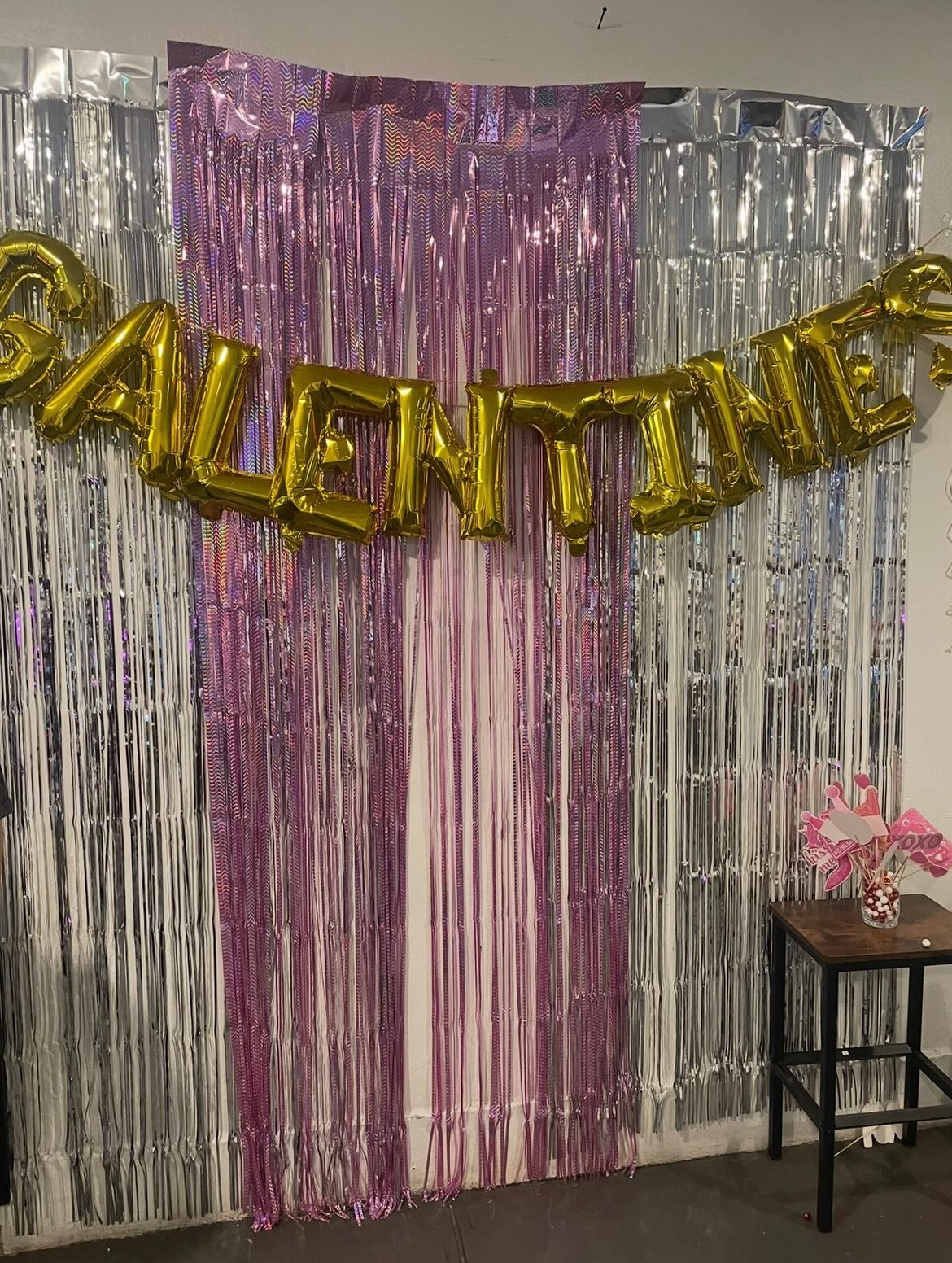 Wall decoration of streaming metallic ribbons and inflated balloon letters reading "Galentines"