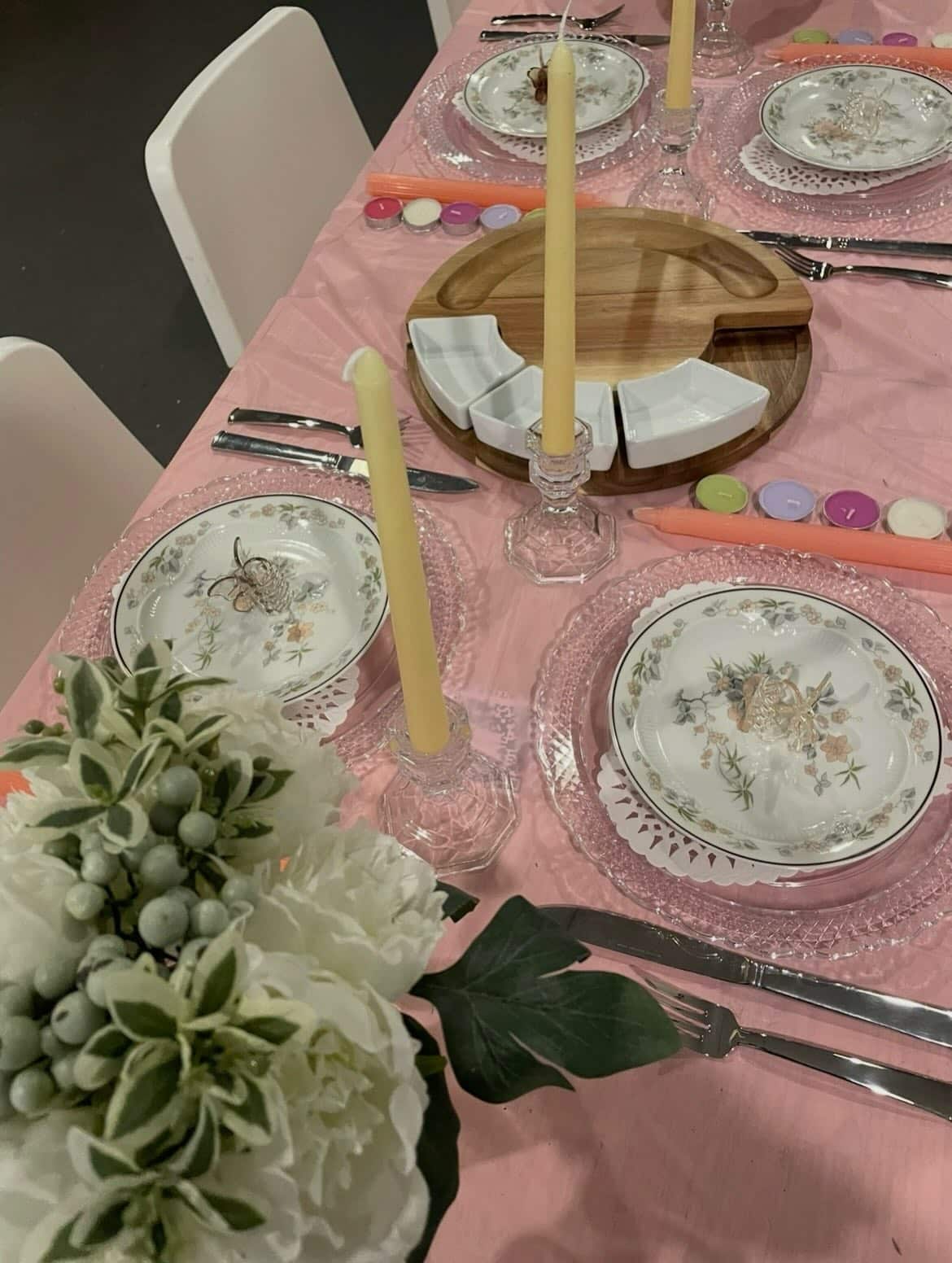 Close up of a place settings on a table with pink tablecloth and flowers for a bridal shower