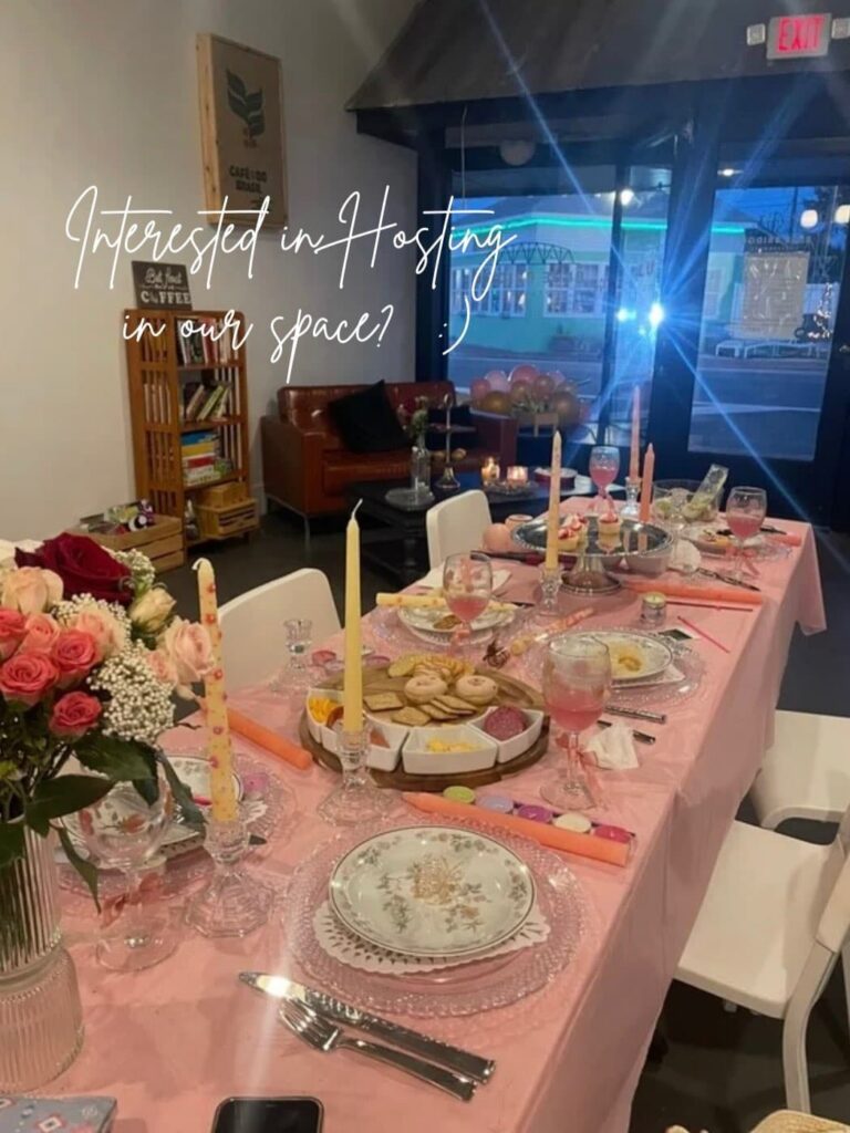 Long shot of a table with pink tablecloth and flowers for a bridal shower with the shop window in the background looking out into the street at night