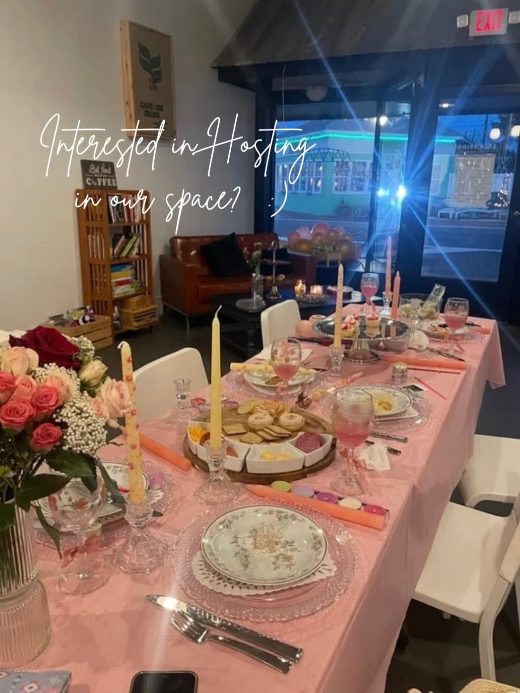 Long shot of a table with pink tablecloth and flowers for a bridal shower with the shop window in the background looking out into the street at night