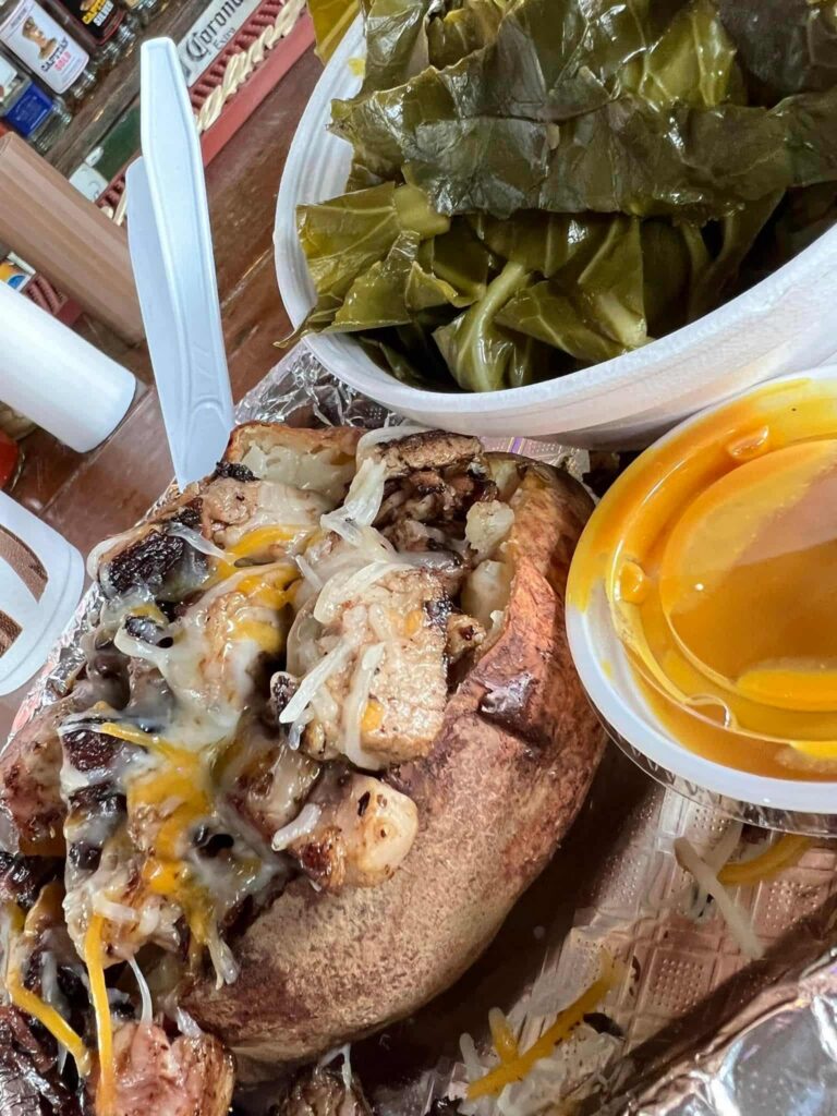 Baked potato loaded with pork barbeque and shredded cheese with a side of steamed greens and a side of BBQ sauce from Captain Stan's Smokehouse