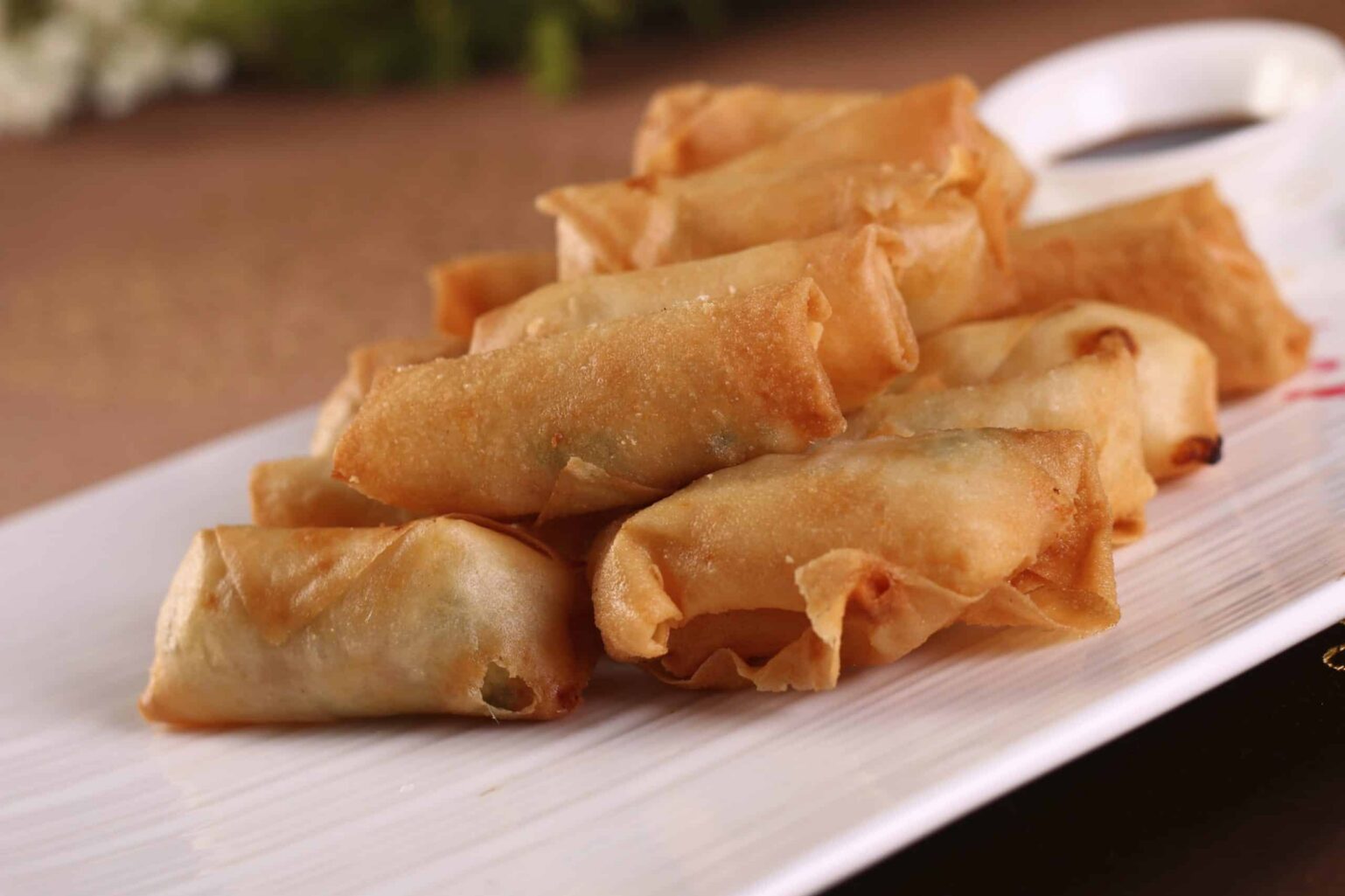 8 or 10 fried spring rolls on a white plate