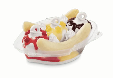 Banana Split in a clear plastic oval bowl with three scoops of ice cream each with a different topping--strawberry, pineapple, chocolate sauce, topped with whipped cream and line with a banana slice lengthwise
