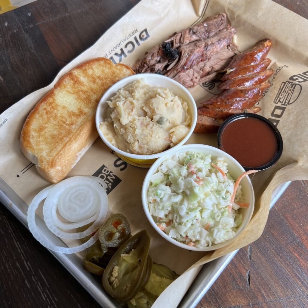 Dickey's BBQ meal with pulled pork, kielbasa sausage, baked potato casserole, cole slaw, sliced white onions, sliced jalapenos, and slice of toasted bread