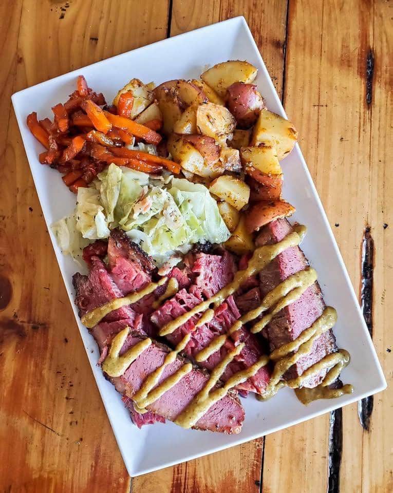 Rectangle white dinner plate of corned beef and cabbage with cubed red potatoes and glazed julienned carrots