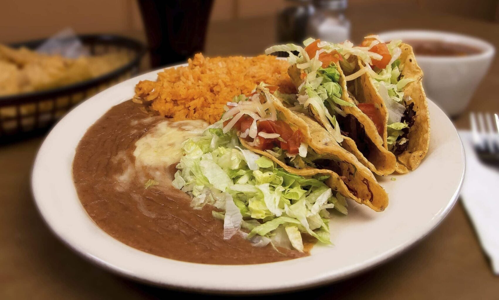Two tacos, refried beans with cheese, Mexican rice and shredded lettuce on a plate at Mi Casa Restaurant