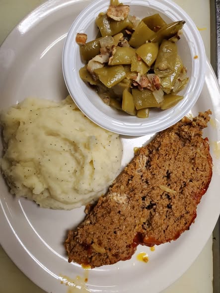 Plate with a slice of meat loaf, a serving of mashed potatoes and side dish of cooked green beans