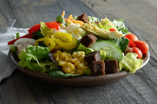 Green salad from Ruby Tuesday salad bar with spinach, romaine lettuce, tomatoes, sliced banana peppers, roasted corn, sliced cucumber and artichoke hearts