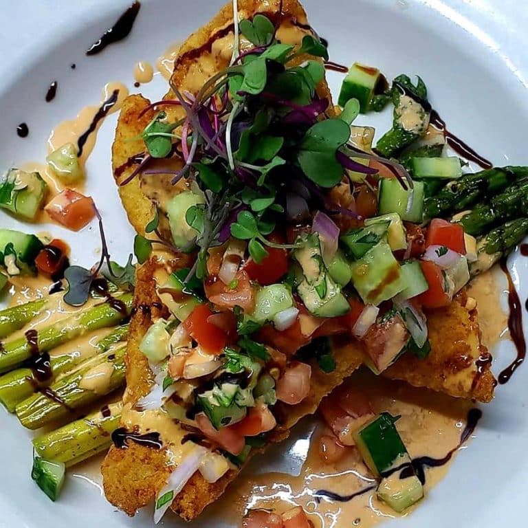 Fried fish on a bed of asparagus topped with cucumber tomato and remoulade, all on a white plate at Seagle's Restaurant