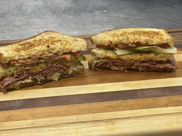 Two halves of a toasted Reuben sandwich on a stripped cutting board