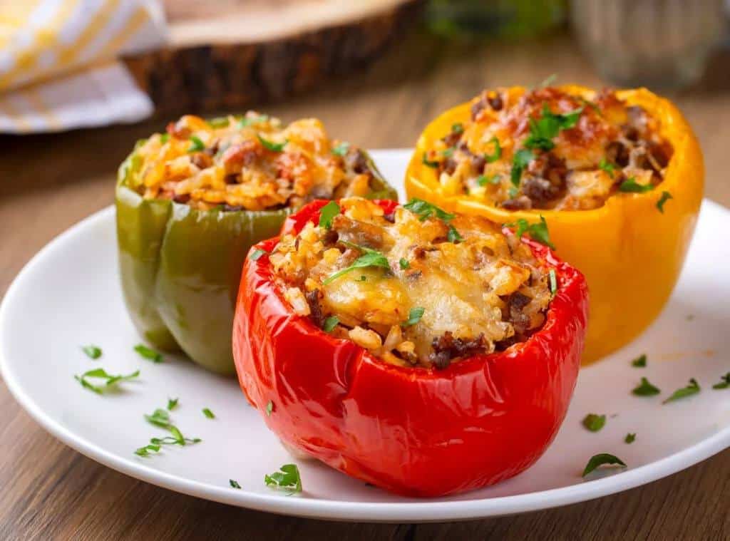 Three bell peppers (red, green and yellow) stuffed with meat and cheese on a white plate