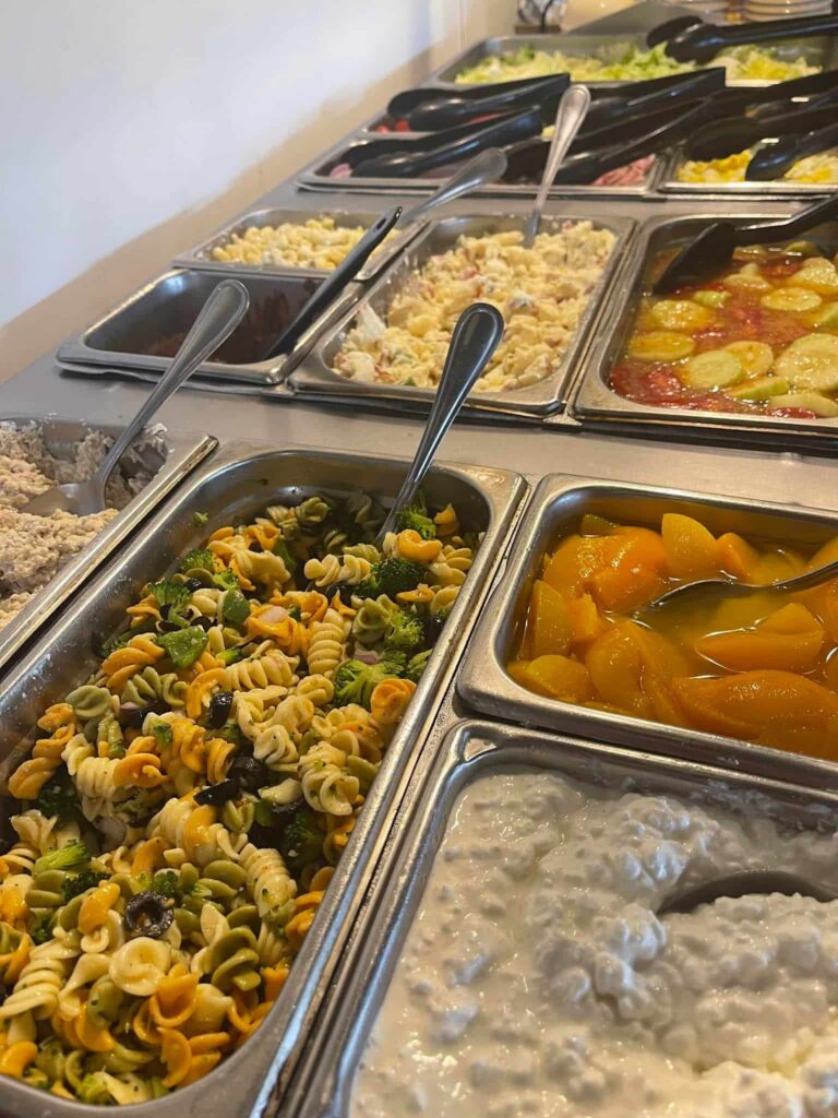 Stainless steel salad bar with pasta salad, cottage cheese, peaches, tuna salad, and more