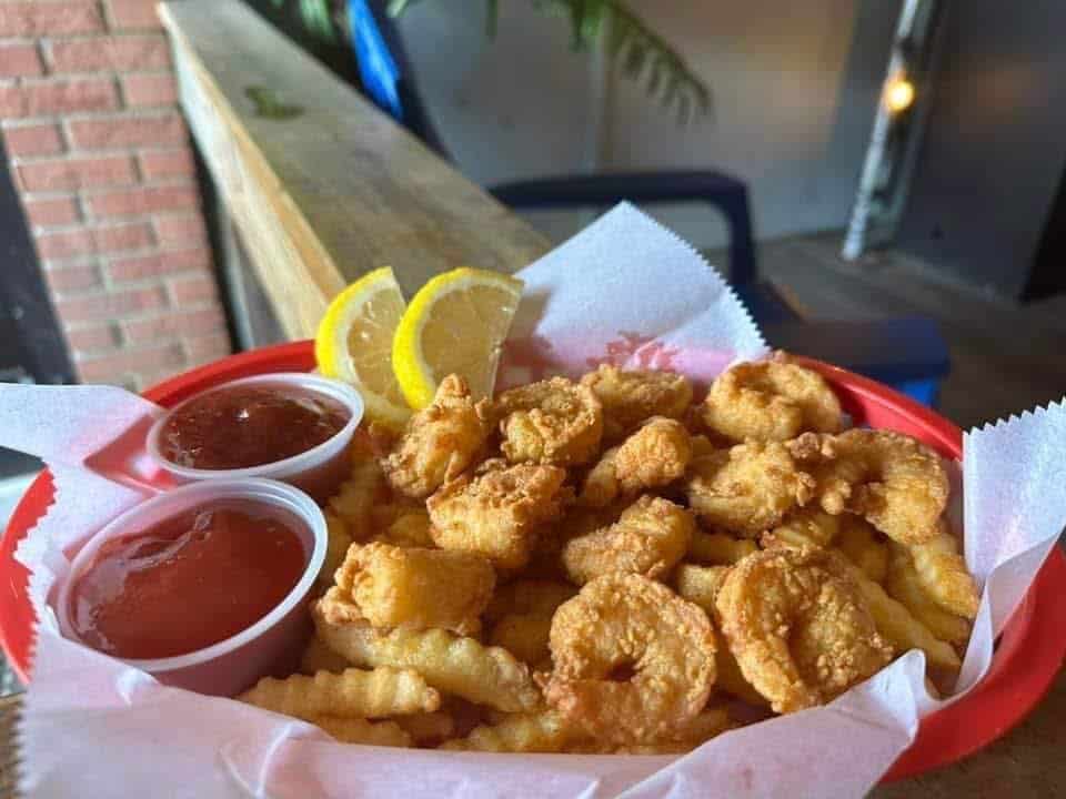 Basket of fried shrimp and fries with sides of ketchup and cocktail sauce with two lemon wedges