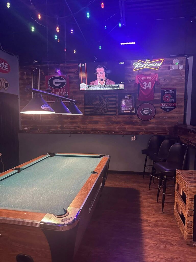 Pool table in a bar with a large, wall-mounted television in the background