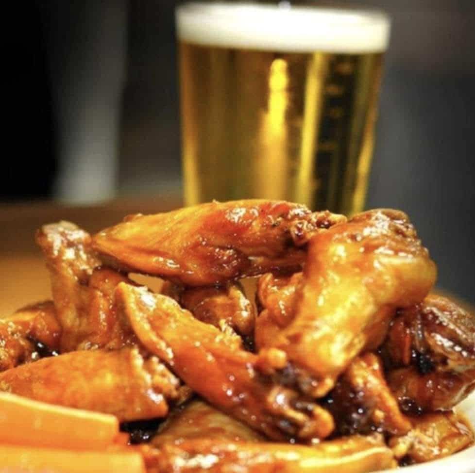 Chicken wings piled on a plate with a glass of beer in the background