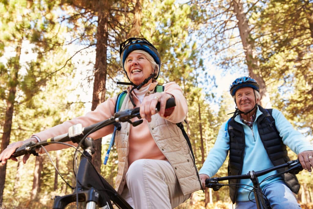 older couple smiling while riding bikes through fall color trees