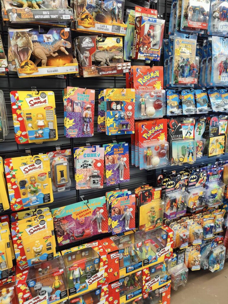 display of packaged action figure toys including dinosaurs, The Simpsons, Pokemon, and Batman branded items