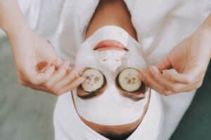 woman smiling with facial mask and cucumbers over her eyes