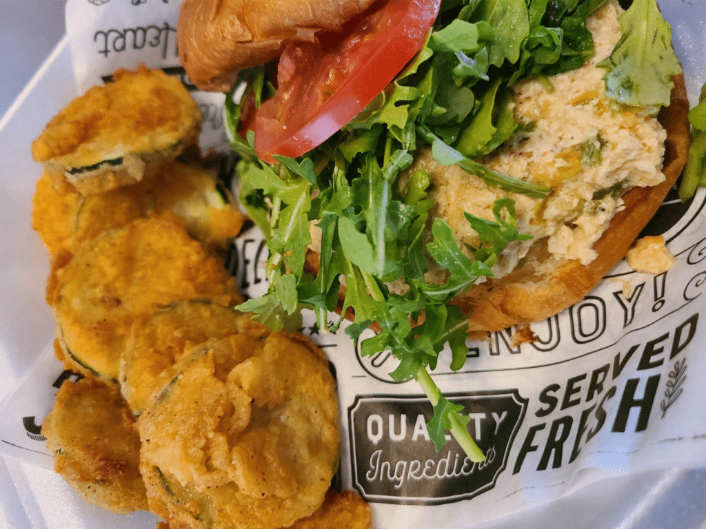 Crabcake sandwich on a roll with lettuce and tomato and aioli sauce with a side of fried zucchini chips