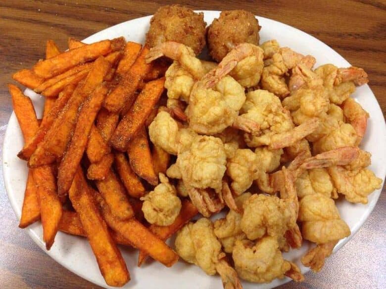 White plate with batter fried shrimp, a pile of sweet potato fries, and two hush puppies from Ship 2 Shore Seafood
