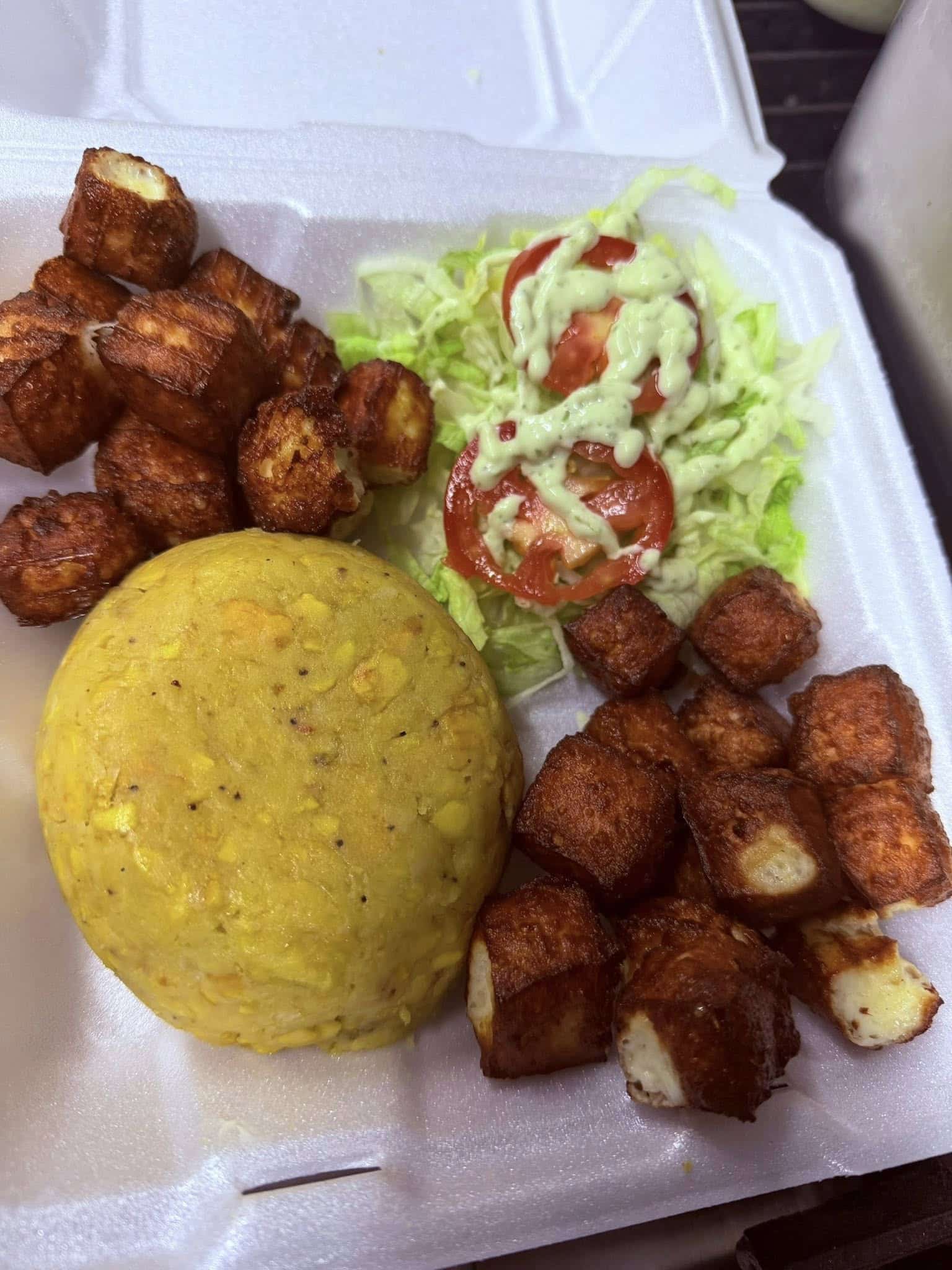A Styrofoam box container of mufungo, fried cheese cubes and a side of shredded lettuce and slice tomatoes