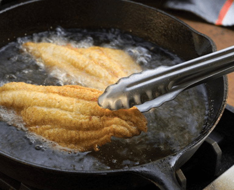 Fish filets frying in a cast iron pan at Sandy's Kitchen