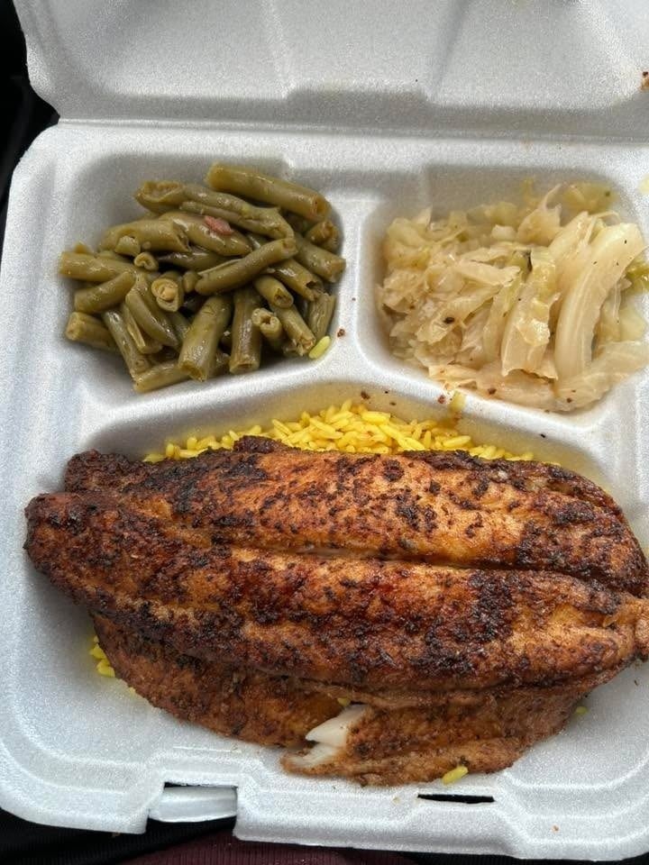 Grilled white fish on a bed of yellow rice with sides of green beans and cabbage in a Styrofoam container