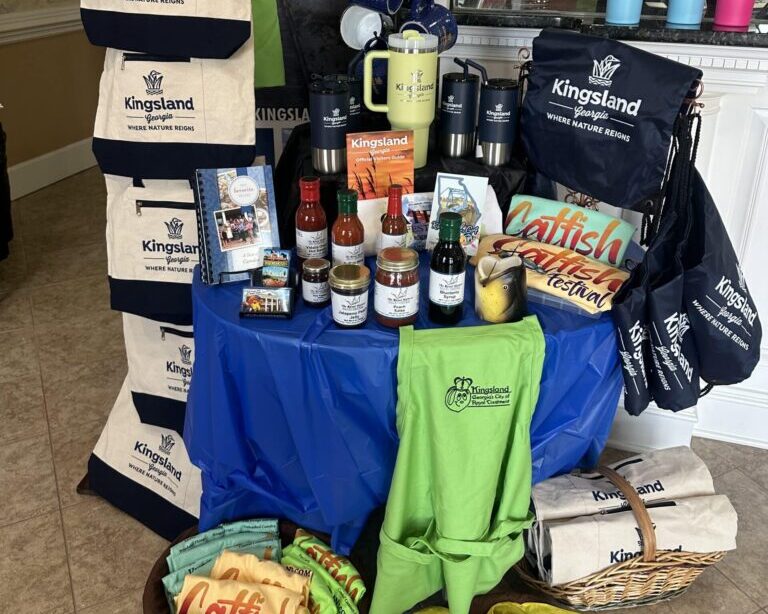 Display of Kingsland, Georgia, branded totes, Stanley cups, and aprons, as well as hot sauces