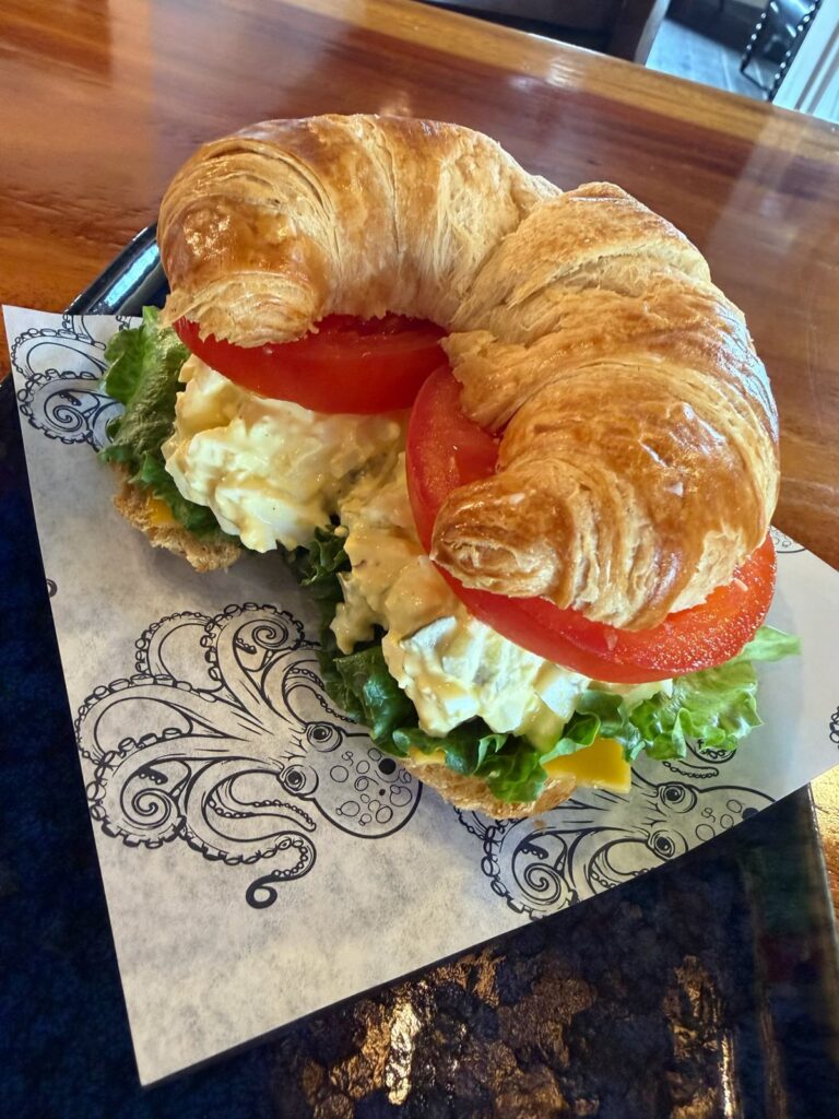 Egg salad sandwich on a croissants with lettuce and tomato on Kraken Coffee-branded parchment paper