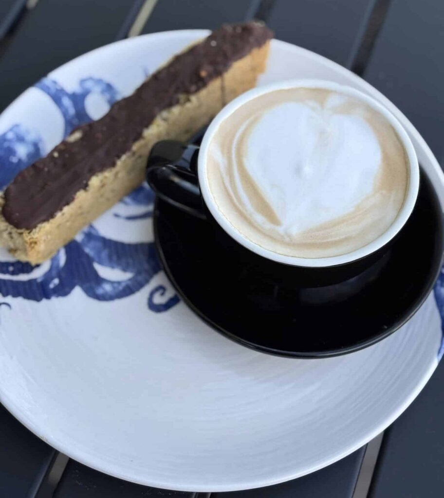 Latte in a black coffee cup on a saucer on a blue and white kraken patterned plate with a slice of biscotti