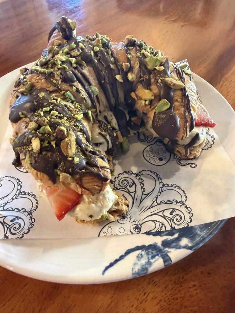 Croissant with strawberries, chocolate syrup, and pistachios on a decorative plate