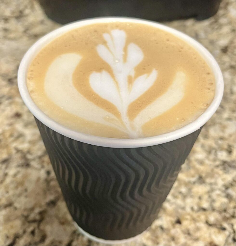 Latte with foam art in a to-go cup on a granite countertop.