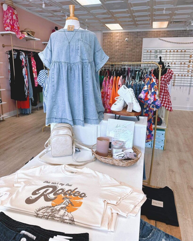 Interior shot of Boutique EllaPar with T-shirts, and gift items on a table, a chambray shirt on a partial mannequin, and a rack with clothing in the background