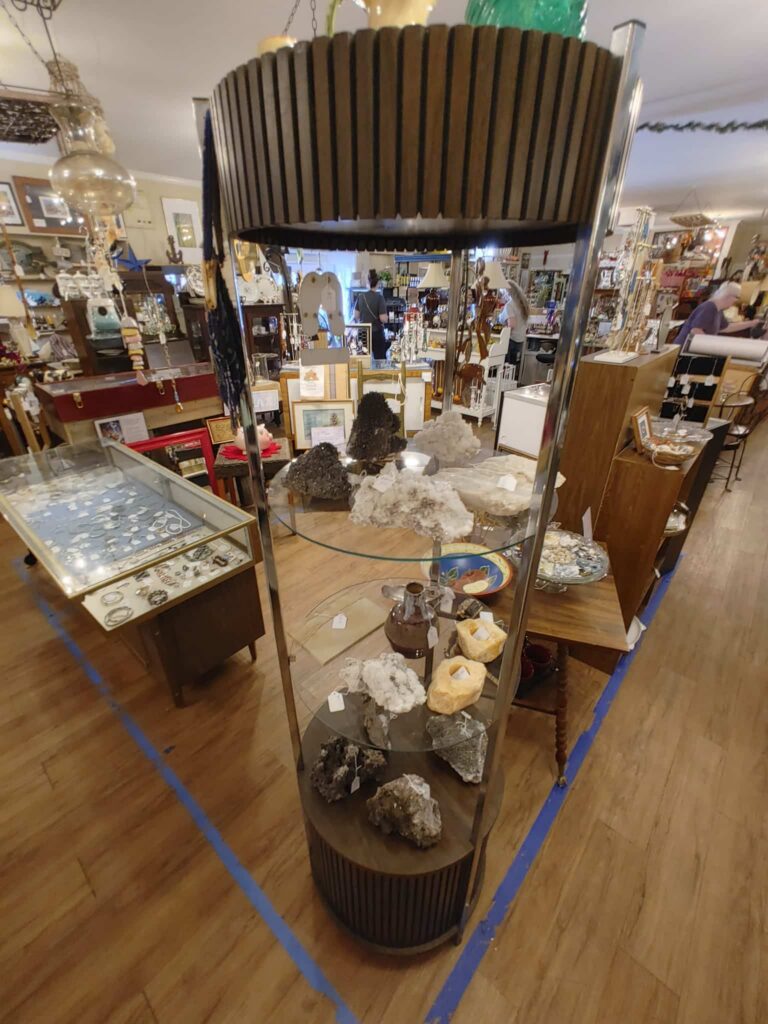 Three-tiered round glass and wood shelf display of rocks and gems with other gift displays in the background
