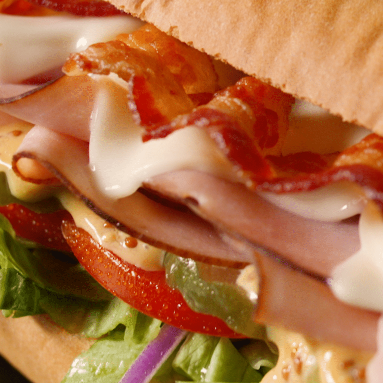 close up of turkey and bacon sandwich with lettuce, tomato, pickles, red onion and mayonnaise on white roll