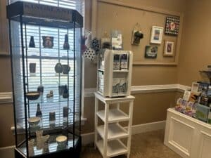Glass cabinet displaying orignal ceramics in front of a window, flanked by a white shelf with brochures in front of a wall hung with original artwork