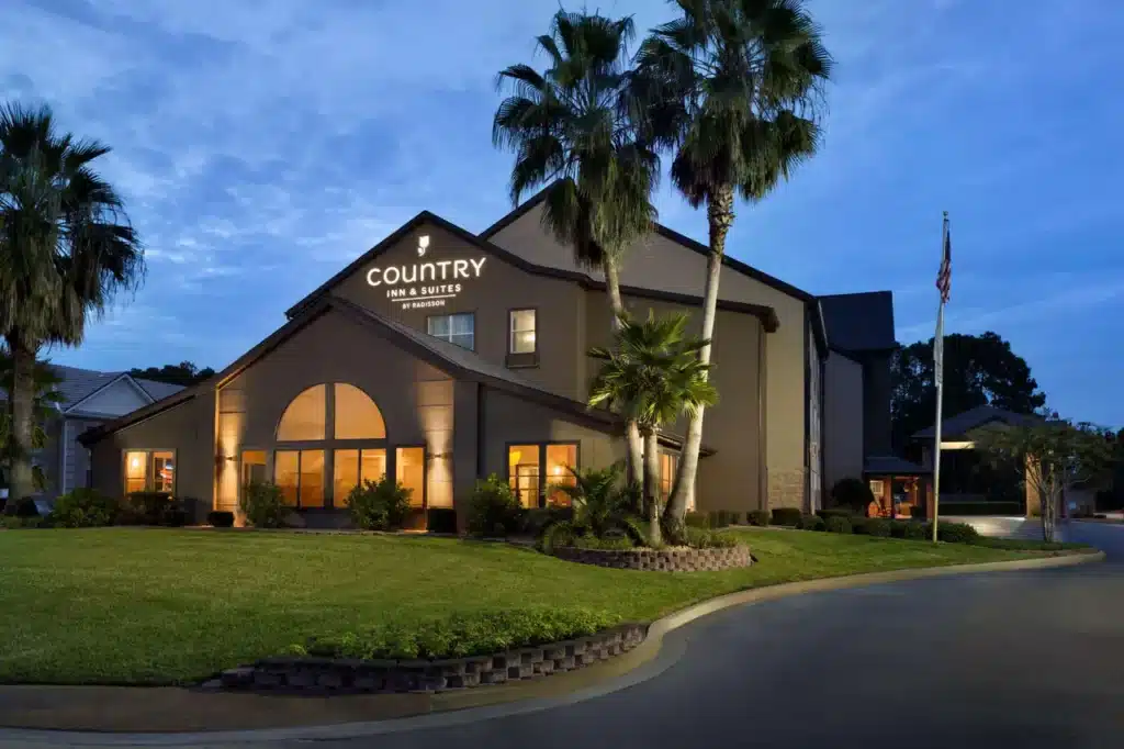 Exterior shot of Country Inn & Suites in Kingsland Georgia in the evening with warm yellow light emanating from the windows of the indoor pool and courtyard