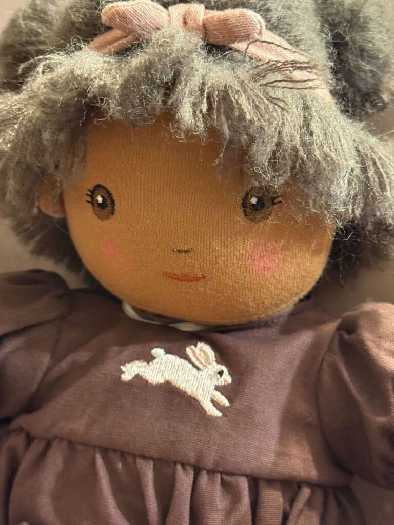 Dolly with brown eyes wearing a brown dress with a white rabbit embroidered on the front