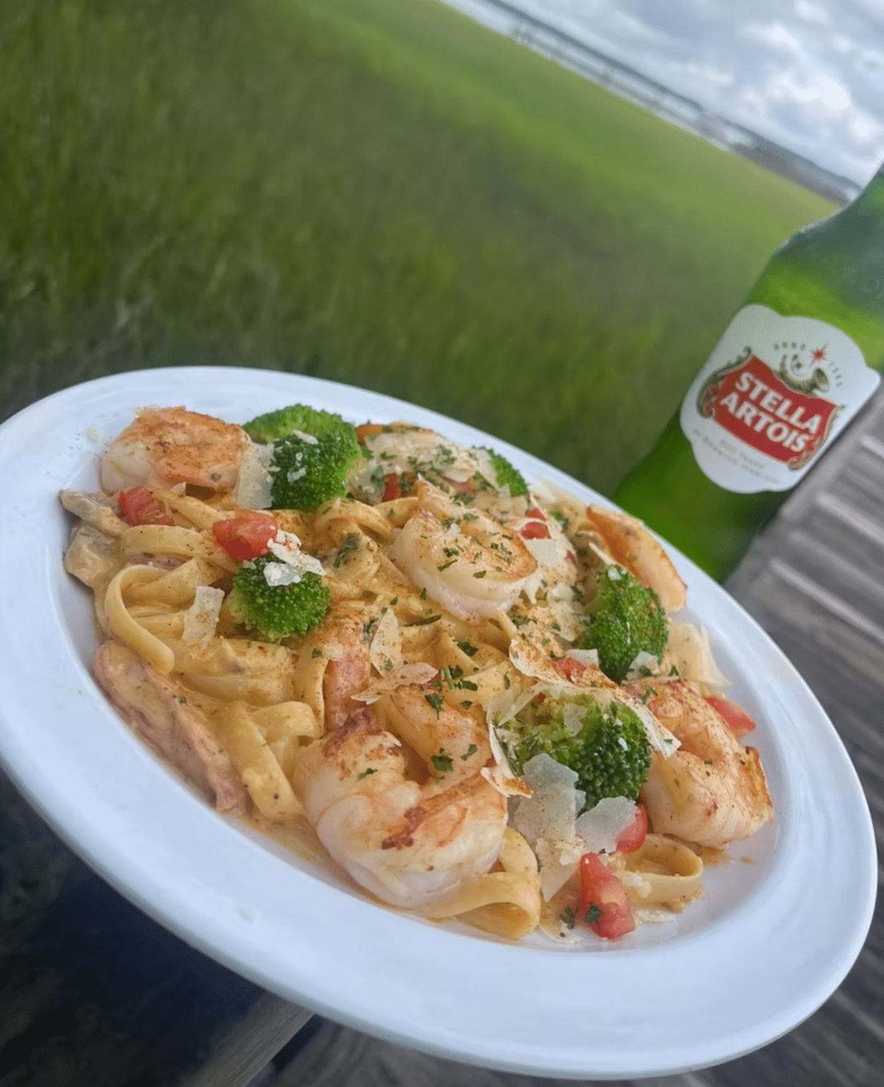 Shrimp & Broccoli Pasta on a white plate accompanied by a bottle of Stella Artois beer against the backdrop of the St. Marys River