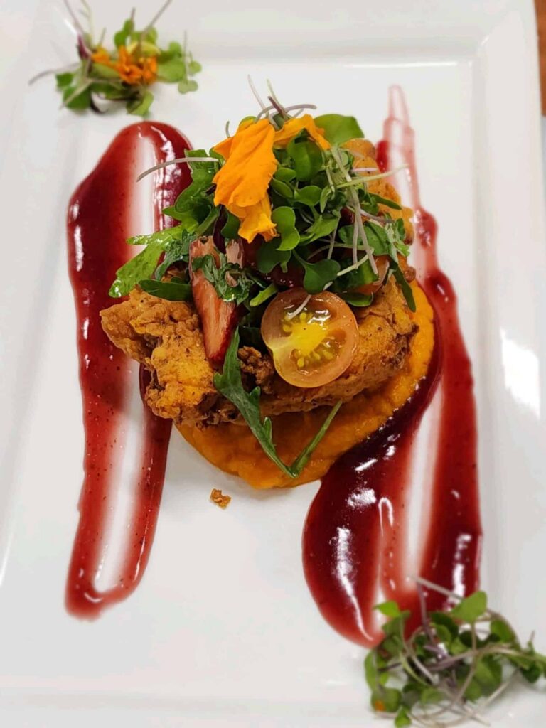 Fried snapper entree on a bed of carrot sweet potato puree topped with tomatos, greens and a strawberry reduction