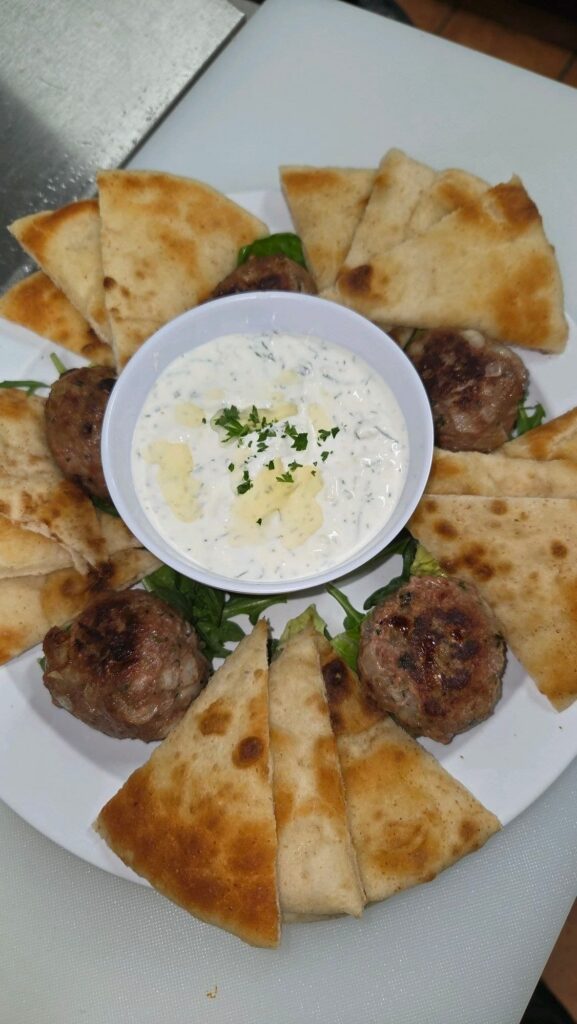 Plate of five Greek meatballs and pita slices with a ramakin of tzatziki in the center