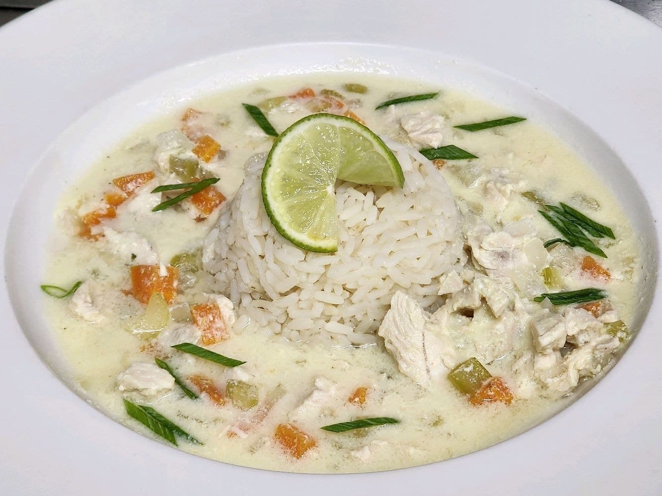 Bowl of chicken lemon soup. A cream colored soup garnished with a lime.