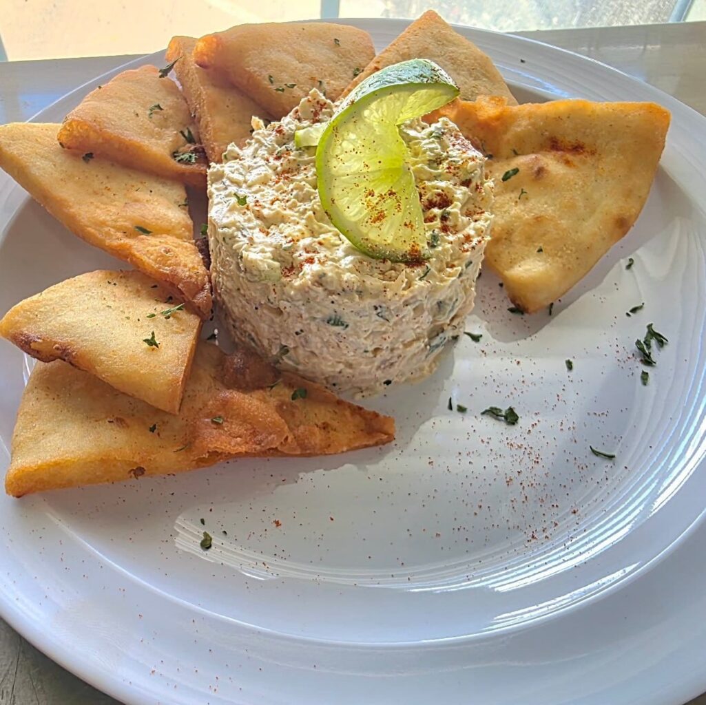 Plate with toasted pita chips and about a cup of fish dip garnished with a twist of lime in the center