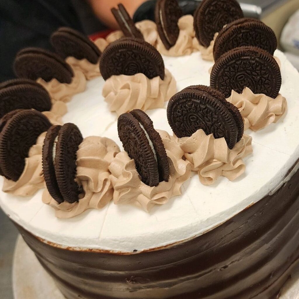 A round cake decorated with 13 Oreo cookies set on their edges like wheels sticking up from the cake.