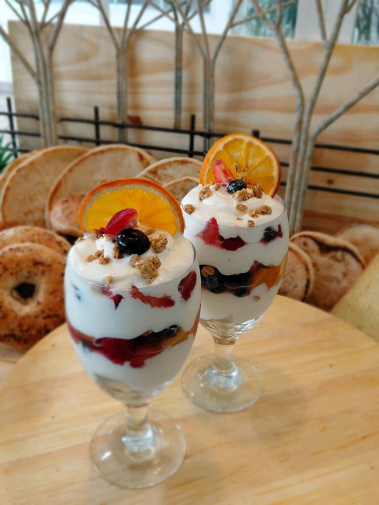 Two fruit and yogurt parfaits garnished with an orange slice in chalice glasses.