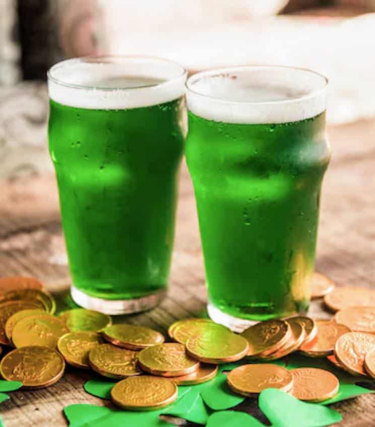Two pints of green beer on a table with gold coins and green shamrock decorations for St. Patrick's Day