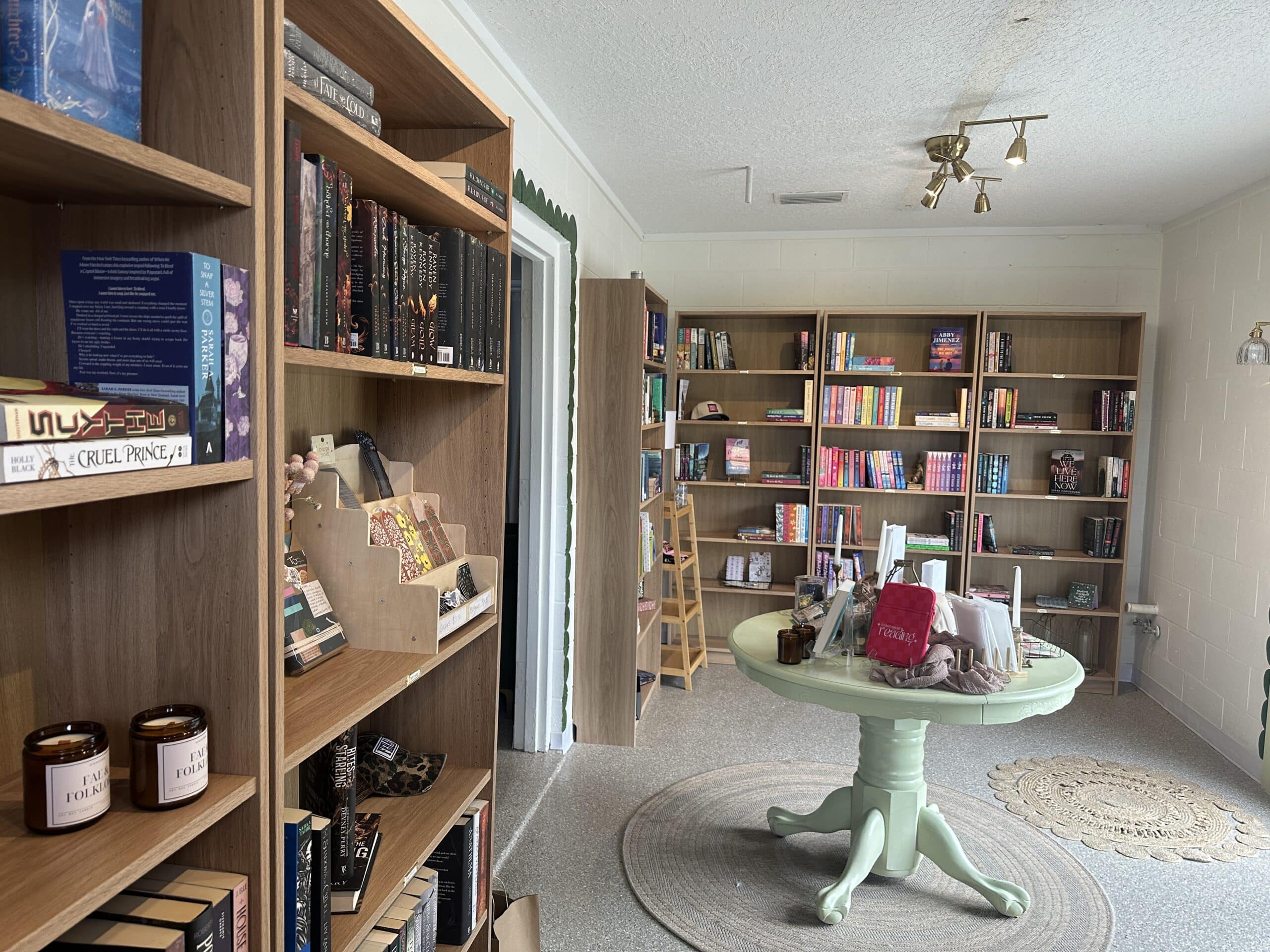 Interior of book and gift shop with wooden Billy bookcases on left and far walls, a round sage green table displaying gift, in natural light
