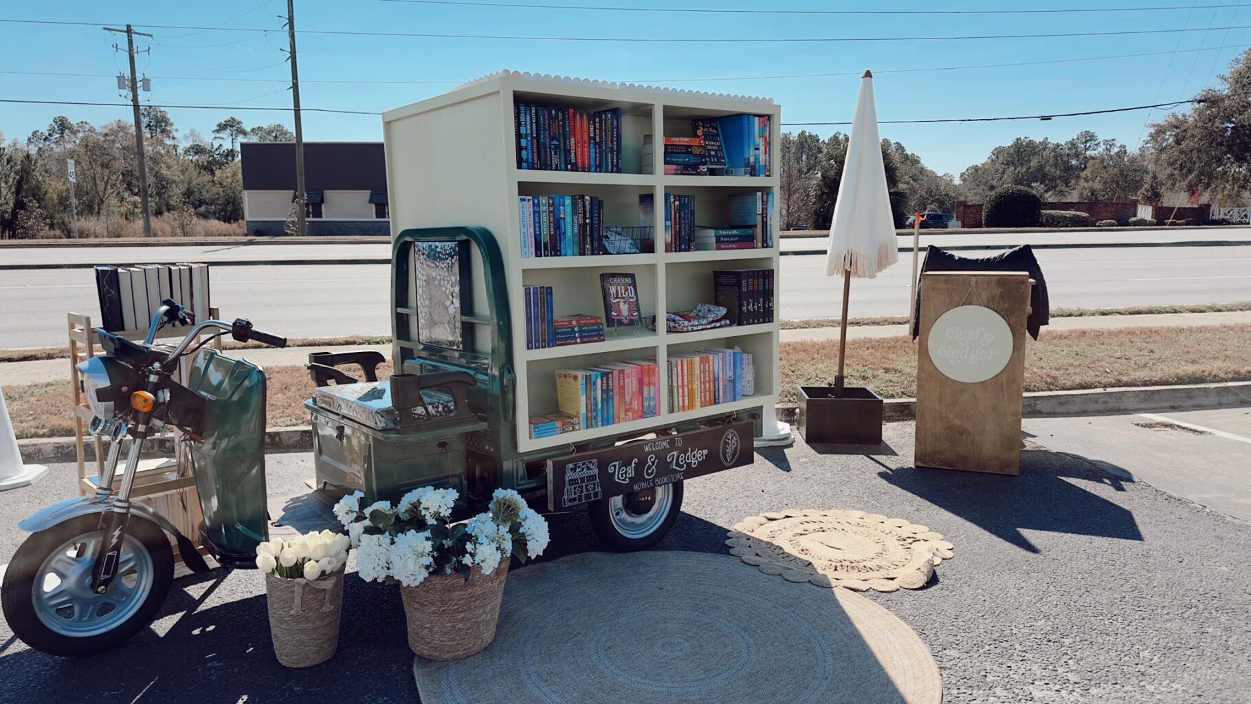 Outdoor shot of Leaf & Ledger Mobile Book Shop on a large outfitted scooter with a large double-sided book shelf on the back