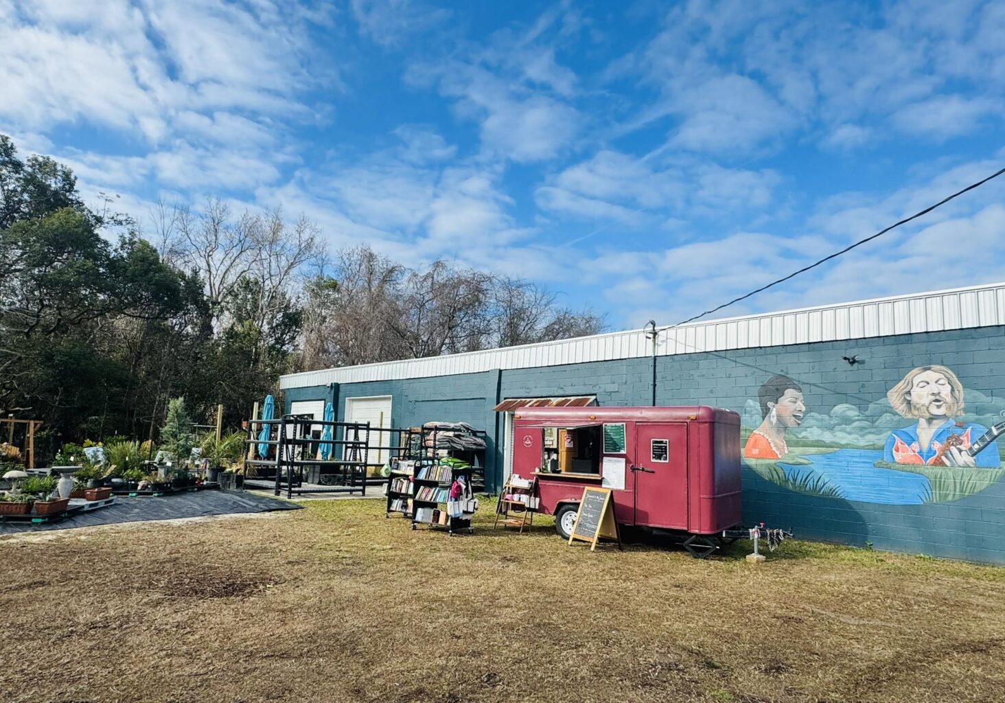 Novel Brews Coffee and Book shop in a red trailer on a sunny day in front of River Tides Outdoor Emporium and Jerry Lee's Music Shop 02-2026
